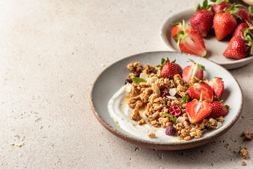Healthy breakfast: fresh granola, muesli with yogurt, strawberry, almond petals and honey on beige textured background. Copy text space