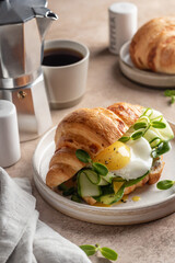 Delisious breakfast with croissant sandwich with fried egg, cheese, cucumber and micro greens and coffee over beige background. Healthy delicious breakfast