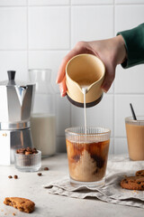 Woman's hand pours cream into glass cup with coffee. Morning traditional coffee and cookies on gray...