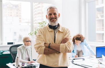 Cheerful man with arms crossed in workspace with colleagues