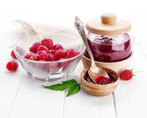 Raspberry confiture in can with fresh berries and leaf on white wooden board, isolated background.