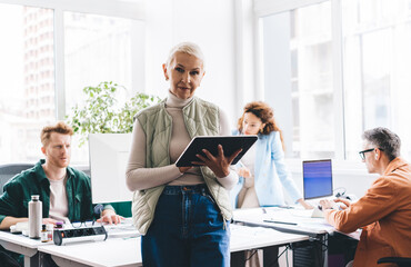 Portrait of confident female entrepreneur holding modern touch pad in hands and looking at camera...