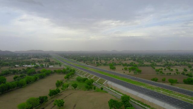 aerial drone slow fly forward over wide deserted delhi mumbai expressway going into the distance with aravali mountains and green feilds on both sides