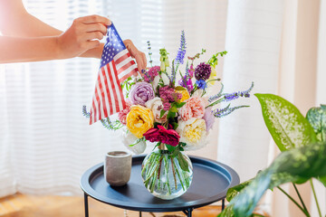 Fototapeta na wymiar Independence day of USA. Woman puts american flag in vase with flowers decorating home. July 4th. Memorial day
