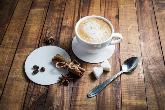 Coffee with spices. Coffee cup, cinnamon sticks, coffee beans, anise, sugar, spoon and coasters on vintage wooden kitchen table background.