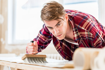Handsome young man applying paste with a synthetic brush to the surface of a wallpaper sheet during...
