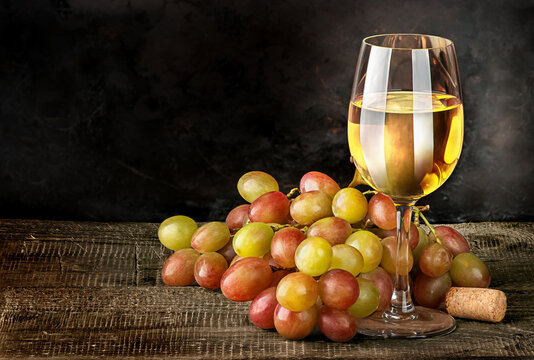 Glass of white wine with grapes on vintage wooden table