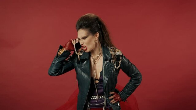 A woman with a dissatisfied face calls on a smartphone, speaks aggressively, shouts into the phone. Angry, frustrated woman freak in the studio on a red background. Advertising.