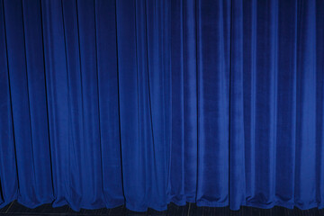 Theatrical curtain is closed, illuminated by spotlights of rich bright blue color.