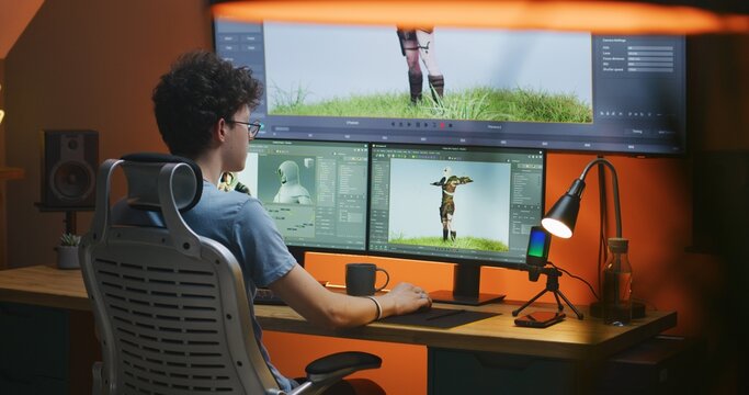 Teenage 3D designer draws video game character, creates animation, works remotely from home in the evening on PC and big digital screen with professional program interface for 3D modeling and design.
