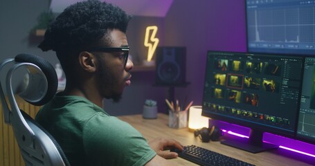 African American colorist edits action movie, makes color correction, works at home. Program...