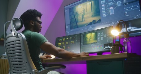 African American video editor makes color grading, works at home office. Computer and big digital screen with program interface with RGB tools and action movie footage. Film post production concept.