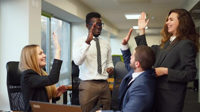 Diverse office corporate workers celebrate successful contract agreement. Multiethnic brokers rejoice about stock market deal victory. Excited business team gives high five about tender, auction win.