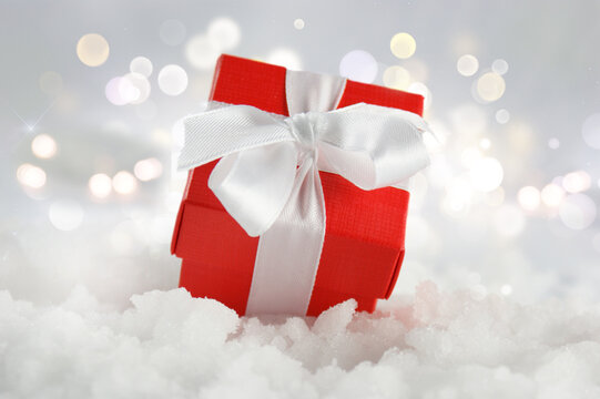 Christmas gift nestled in snow against a bokeh lights background