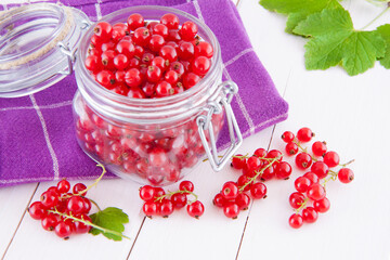 Red currants in a glass jar on a wooden white table