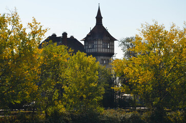 Old half-timbered house with square tower behind some autumn colorful trees on the Main river in Frankfurt