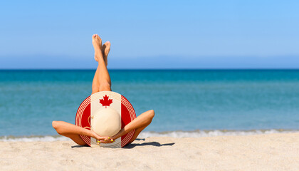 A slender girl on the beach in a straw hat in the colors of the flag of Canada. Focus on the hat.