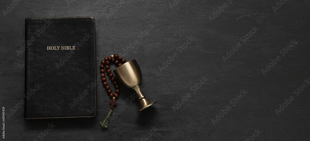 Wall mural Holy Bible, chalice and prayer beads on dark background with space for text