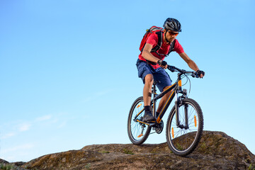 Cyclist in Red T-Shirt Riding the Bike Down the Rock on the Blue Sky Background. Extreme Sport and Enduro Biking Concept.