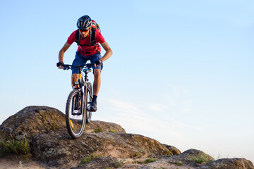 Fototapeta premium Cyclist in Red T-Shirt Riding the Bike Down the Rock on the Blue Sky Background. Extreme Sport and Enduro Biking Concept.