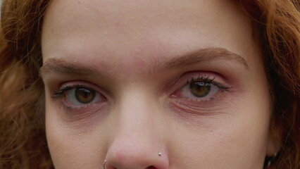 Macro close-up of redhead woman looking at camera with serious expression. A female 30s millennial person eye