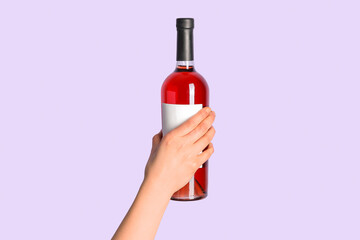 Female hand holding bottle of red wine on lilac background