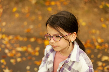 little girl in glasses and plaid shirt in the autumn park.