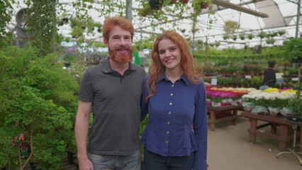A happy redhead couple smiling at camera standing inside flower shop. Caucasian red hair Man and woman inside local store