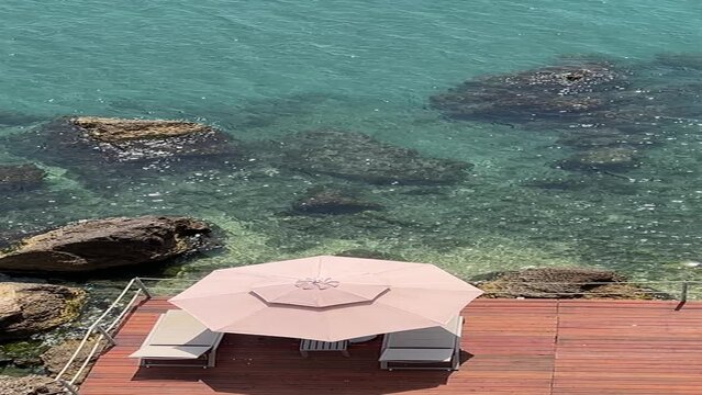 Beach sunbeds and sunshade on sea shore of rocky coast,  vertical video.