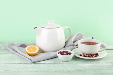 Fototapeta na wymiar Cup of fruit tea, teapot and lemon on green wooden table