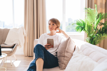 Cheerful adult woman with smartphone in modern apartment