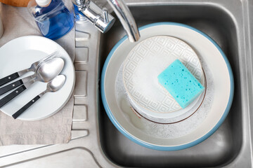 Dishes with cleaning sponge in sink, closeup