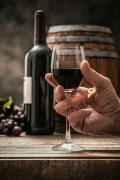 Senior man drinking a glass of expensive red wine in his cellar, wine bottle, grape and barrel on the background, wine tradition and culture concept