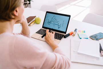 Crop thoughtful woman working on laptop at home at table