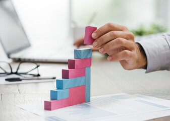 Businessman working at office desk, he is building a growing financial graph using wooden toy...