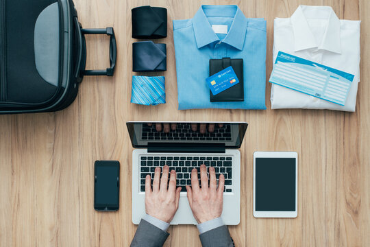 Planning a business trip: corporate businessman packing his bag and using a laptop, travel and technology concept