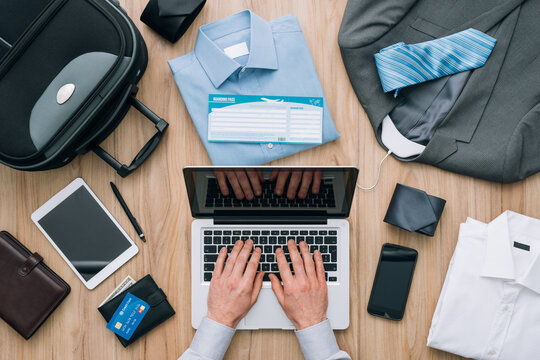 Corporate businessman packing his bag and planning a business trip, he is booking flights online using a laptop, travel and technology concept
