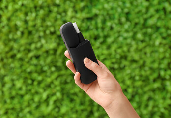 Female hand holding modern electronic cigar with stick against green nature background