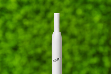 Modern electronic cigar with stick against green nature background