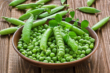 Green peas in ceramic bowl on rustic wooden background