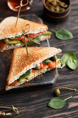 Two club sandwiches with salmon, avocado, capers, cream cheese and baby spinach leaves on vintage wooden cutting board	
