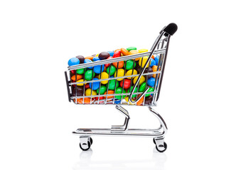 Round coated sweet candies in shopping cart on white background