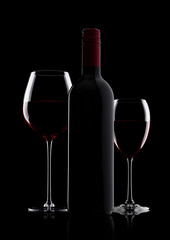 Glass of red wine with bottle with shape on black background with reflection