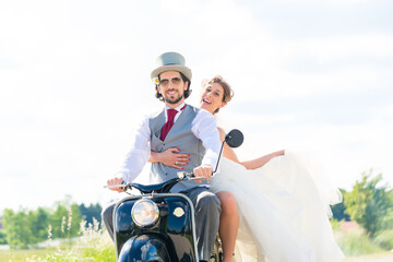 Wedding groom and bride driving motor scooter having fun