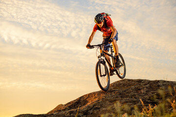 Fototapeta na wymiar Cyclist in Red T-Shirt Riding the Bike Down the Rock on the Sunset Sky Background. Extreme Sport and Enduro Biking Concept.