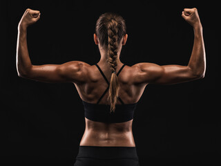 Fototapeta na wymiar Studio shot of a fit young woman showing her muscles, against a dark background
