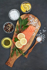 Obraz na płótnie Canvas Fresh salmon fish with herbs, seasoning, olive oil and lemon fruit on marble slab on slate background. Healthy heart food high in omega 3 fatty acids.