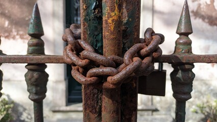 The old rusty gate is closed and wrapped with a thick steel chain with a lock