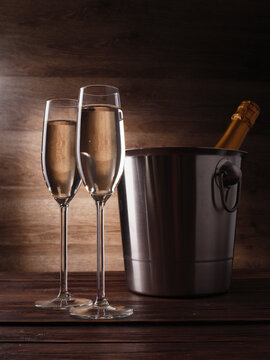 Image of two wine glasses with champagne, steel bucket and bottle on wooden background