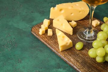Wooden board with tasty Swiss cheese on green background